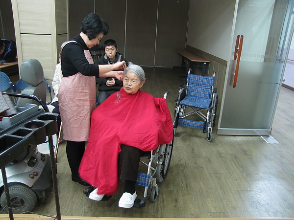 휠체어에 앉은 어르신을 커트하는 여자 봉사자분